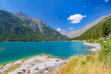 Obraz premium Ceresole Reale, Italy. View of Lake Ceresole on a sunny summer day. Some people sunbathing on the lake shore. Alps mountains in the background. Mountain landscape. 2023-08-20.