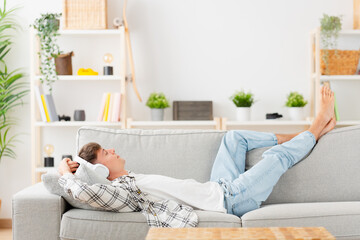 Caucasian teenager lying on sofa. Young man relaxing while listening to music.
