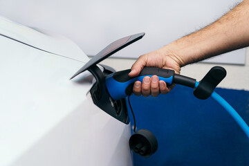 unrecognizable Male hand with visible forearm hair plugging in a blue electric charger into the...