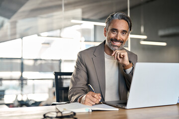 Happy middle aged professional business man, older executive ceo manager, smiling mature entrepreneur lawyer wearing suit sitting at office desk working on laptop computer. Copy space. Portrait.