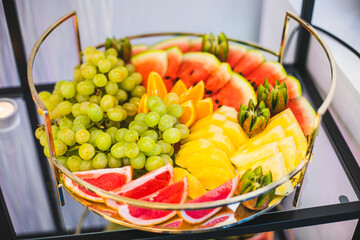 Round dish with variety of fresh fruits on buffet table at festive event. Mini snacks and treats. 