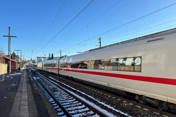 An electric train departing from the station platform. Clear blue sky.