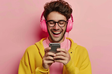 Joyful positive young man on pastel studio background uses mobile phone and noise cancellation headphones head set, listens to music, has good time, enjoys his favorite tracks