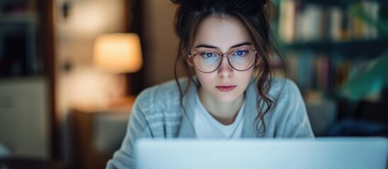 A girl with glasses is working on her laptop, struggling to read online content due to eyesight issues.