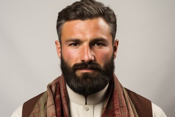 Portrait of a handsome young man with a beard wearing a brown vest and a red scarf. - Powered by Adobe