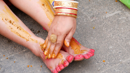 Haldi ceremony in hindu marriage, applying haldi or turmeric paste on feet of a bride.