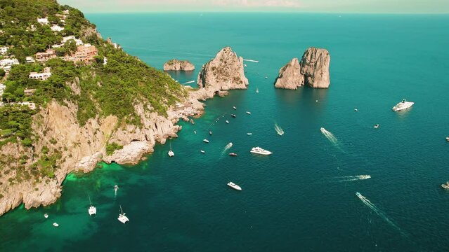 Majestic Aerial View of Rocky Seaside and Luxury Boats Sweeping. Iconic rock formations Faraglioni emerge from azure sea of Capri, Italy.