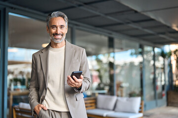 Happy mature older business man entrepreneur wearing suit using mobile cell phone outdoors. Middle...