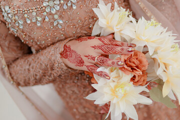 The bride's hands are holding flowers and wearing henna. Indonesian wedding with brown kebaya dress