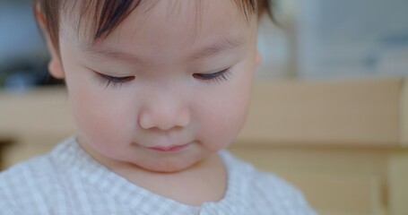 Intimate close-up of a pensive toddler with eyes cast down, in a soft-focus indoor environment.