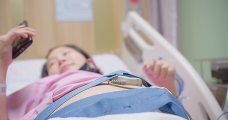 Pregnant woman lying in a hospital bed, fetal monitor strapped to her belly, Pregnant woman in...