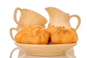 Two delicious eclairs on ceramic saucer with cups and milk jug, macro, isolated on white background.