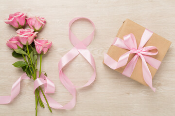 Composition with pink roses, gift box and eight made of ribbon on wooden background, top view. Women's day concept