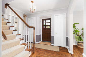 An entryway with a wood and white staircase, gold light fixture, and a wooden front door.