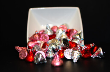 A white bowl tipped over spilling assorted chocolate candy.