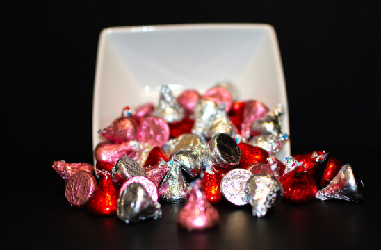 A white bowl tipped over spilling assorted chocolate candy.