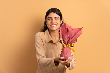 cheerful brazilian woman offering easter egg in beige colors. holiday, easter, celebration concept.