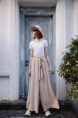 A young girl dressed in wide trousers and a hat walks through the old city. - 738244207