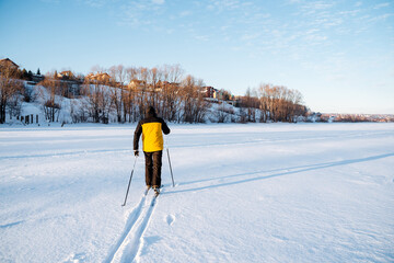 Rear view of skier walking on field in winter, man laying trail on deep snow. A lonely traveler in...
