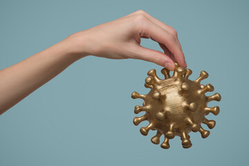 A woman's hand holds a gold-colored virus model. Blue background. - 738246817