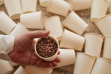 A hand holding a paper cup with coffee beans among empty cups. Fresh coffee beans, donate for coffee