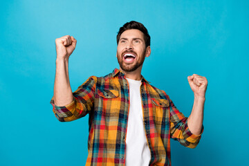 Photo portrait of attractive young man raise fists win lottery dressed stylish checkered clothes isolated on blue color background
