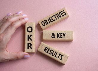 OKR objectives and key results symbol. Wooden blocks with words OKR objectives and key results. Businessman hand. Beautiful pink background. Business and OKR concept. Copy space. - obrazy, fototapety, plakaty
