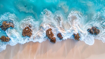Aerial drone view of waves hitting rocky shore with clear turquoise water on beach.