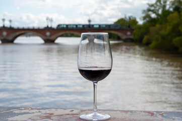 Tasting of Bordeaux blended red wine with wine city Bordeaux on background, left bank of Gironde Estuary, France. Glass of red French wine.