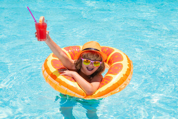 Child in sunglasses and summer hat drink summer cocktail and floating in pool. Cute little boy in...