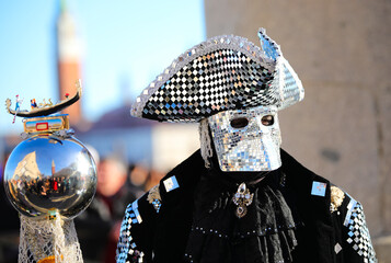 Venice, VE, Italy - February 13, 2024: masked person with huge hat with mirrors and sequins and a sphere with the gondola