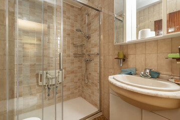 Image of a bathroom with cream-colored furniture, a tiled wall with various cream-colored tiles and...