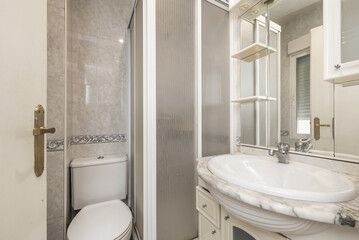 Image of a bathroom with white furniture, a tiled wall with blue borders and a white cabinet with...