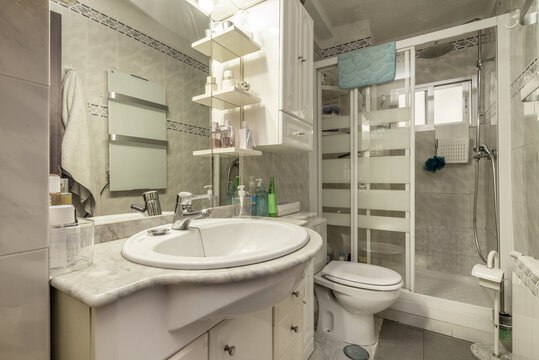 Image of a bathroom with white furniture, a tiled wall with blue borders and a white cabinet with integrated mirrors and a square shower cabin