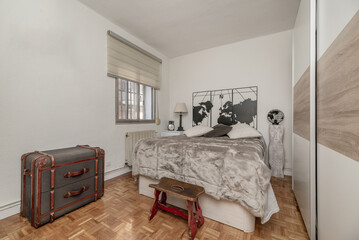 Bedroom with a large bed that occupies the entire space, a shoe-removing armchair, a vintage travel...