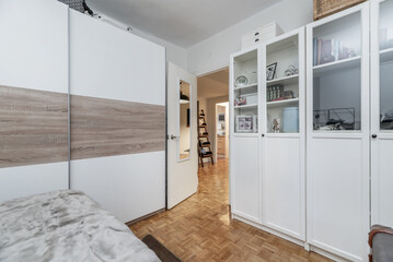 Bedroom with a large bed, white wardrobes with a display case and a wardrobe with wooden and white...