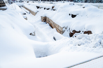 A pit with a pipeline under a layer of snow, city communications for water supply to the...