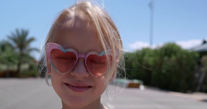 Close up of a smiling 6-year-old girl in heart-shaped sunglasses, missing her front teeth