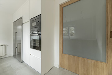 kitchen with white wooden furniture with appliance column, large wooden door and matching...