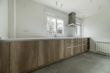 Image of a kitchen with wooden furniture, white synthetic stone countertop, stainless steel extractor hood, several windows and white aluminum radiator