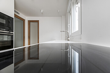 Image of a kitchen with wooden furniture, white synthetic stone countertop, sink with chrome faucet and glossy black ceramic hob