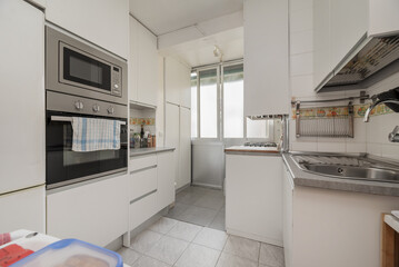Image of a small kitchen with all the walls covered in white furniture and integrated appliances