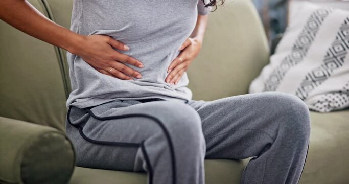 Home, closeup or woman with period pain, sick and digestion problem with menstruation in a living room. Person, apartment or girl in lounge, endometriosis or holding belly for cramps, sick or illness