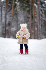 Cute child baby eat bagel in a plush fur coat and a hat with ears in a snowy winter forest