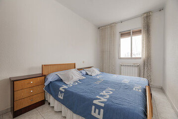 Fototapeta na wymiar Bedroom with two single beds with blue bedspreads, old wooden furniture and an aluminum window with white curtains