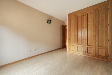 An empty room with a built-in wardrobe covering a wall with floor-to-ceiling wooden doors