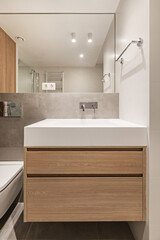 Frontal image of a small modern bathroom with an elongated white stone imitation sink with a wooden...