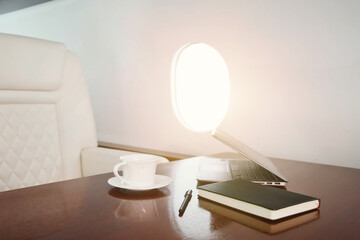 Comfort vip interior salon private jet with laptop, diary, coffee cup on table, at highest. Luxury...