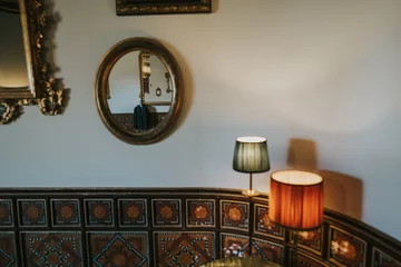 Foto op Canvas Espejo redondo y dos lámparas de sobremesa en un salón. A través del espejo vemos la chaqueta de un traje de hombre colgada de la percha. © Ruben