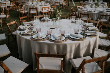 
Banquete al aire libre. Mesa redonda decorada en tonos ocres y rosas. Vajilla de porcelana, mantelería de mimbre y cristalería en varios tonos.